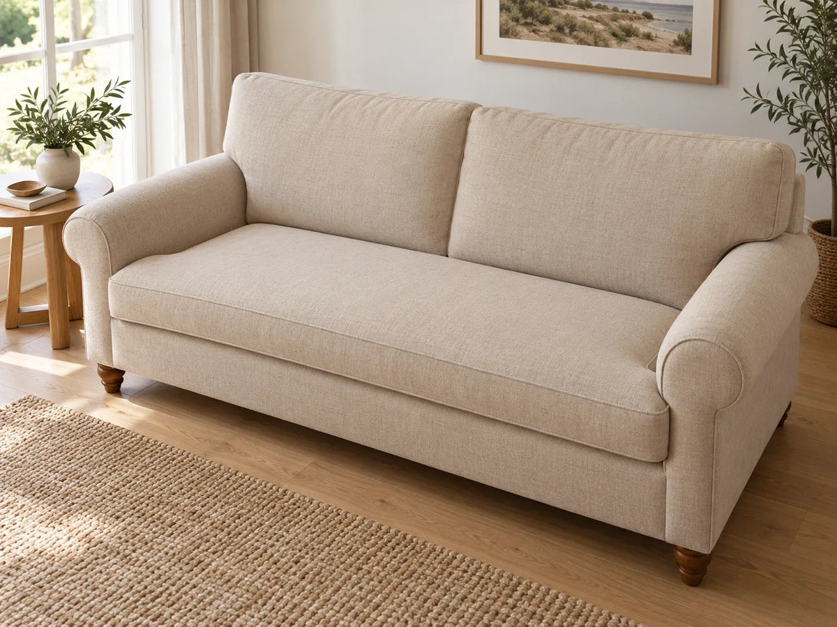 An oat upholstered sofa with a broad loose bench seat cushion, rounded arms and two back cushions in a sunlit living room.