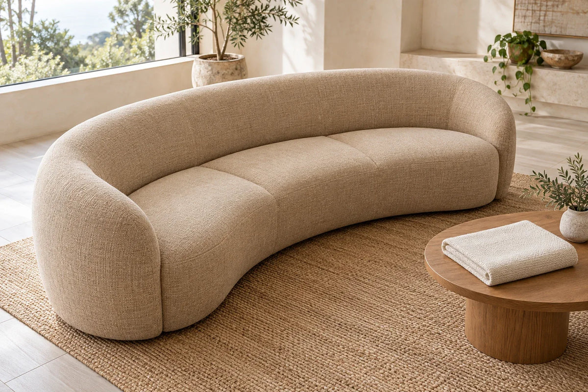 Uncovered sand-coloured curved sofa, with a folded rectangular ivory cover resting separately on a round side table.