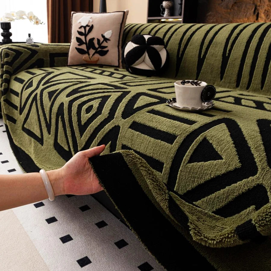 Hand lifting the edge of a green Valencia throw with black geometric patterns on a sofa