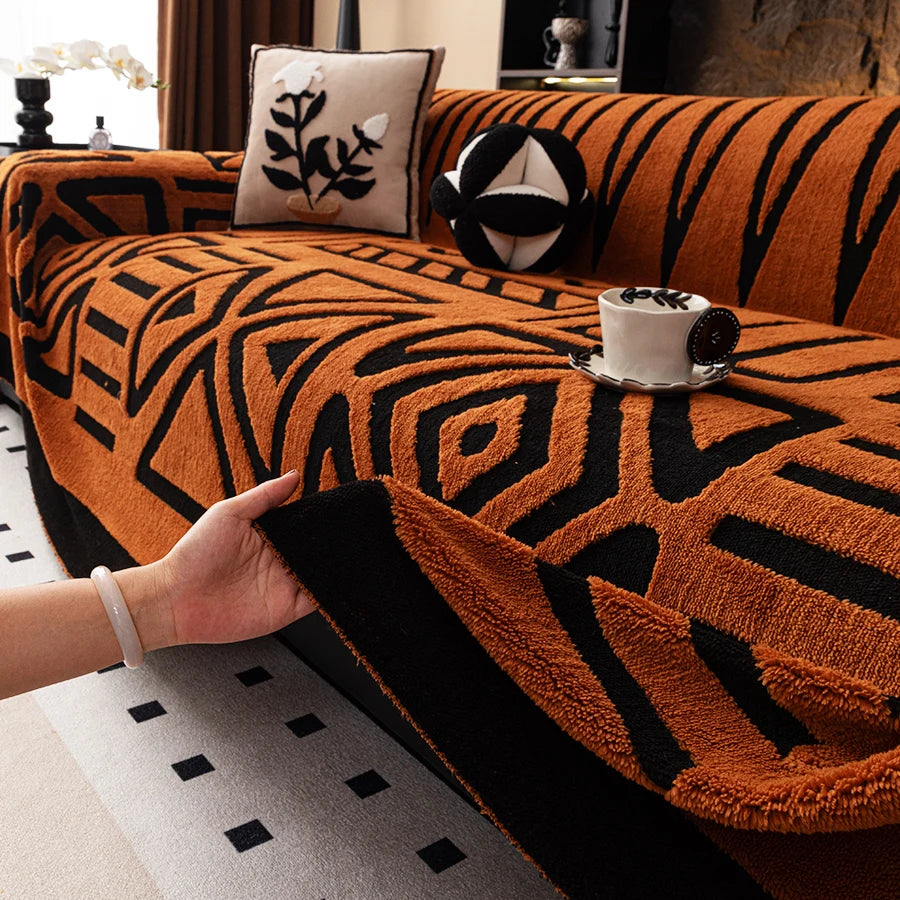 Hand lifting the edge of an orange Valencia throw with black geometric patterns on a sofa