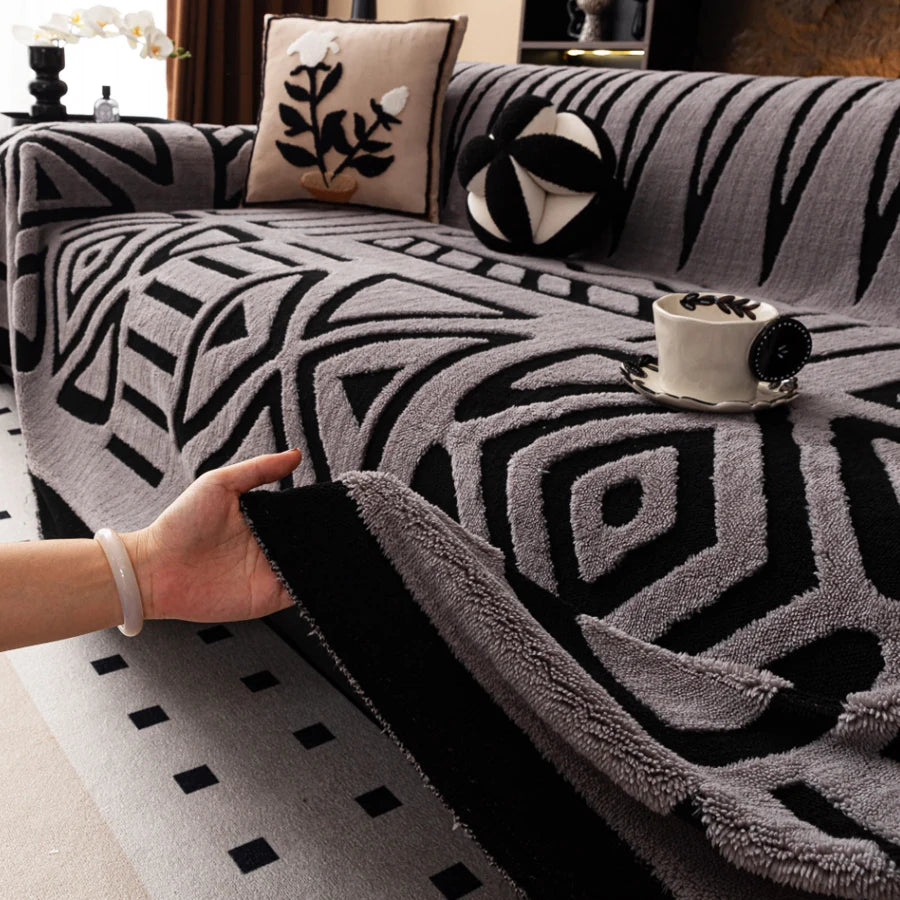 Hand lifting the edge of a light grey Valencia throw with black geometric patterns on a sofa
