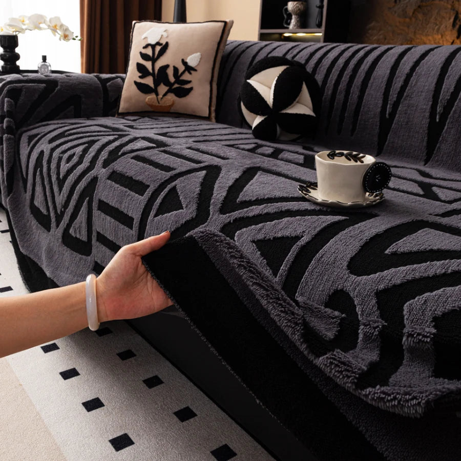 Hand lifting the edge of a dark grey Valencia throw with black geometric patterns on a sofa